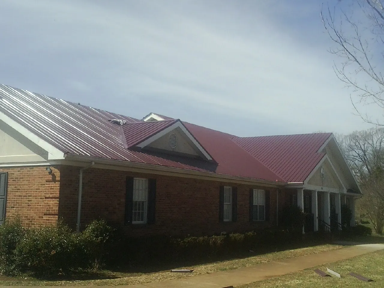 Red metal roof with gabled entries on a long brick building, from a Hail Damage Roof Repair job in Anvik