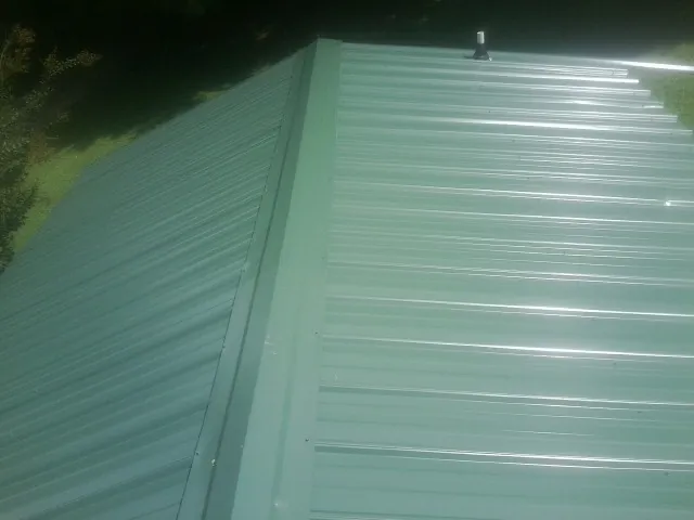 New green metal panels meeting at the ridge of a roof — Flat Roof Repair work by our crew in Anvik