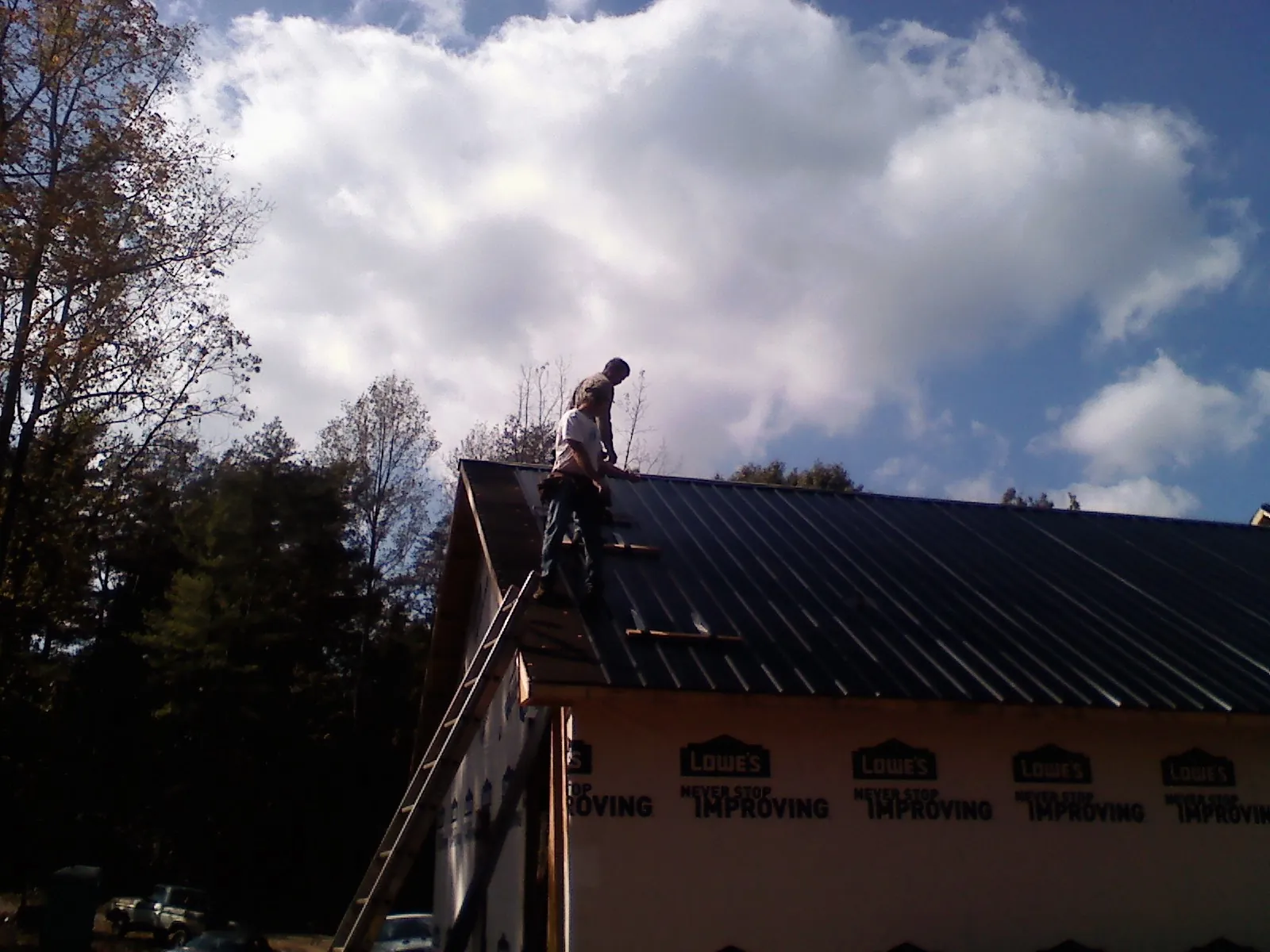 Roofer fastening dark metal panels high against a cloudy sky, from a Roof Inspection job in Anvik