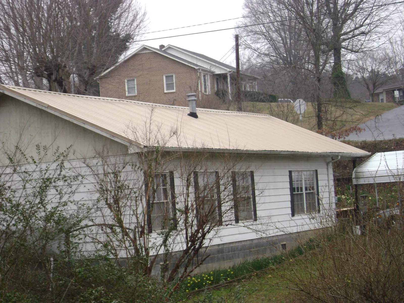 Tan metal roof on a white sided house set into a hillside — Commercial Roofing by Roofing Brothers in Anvik