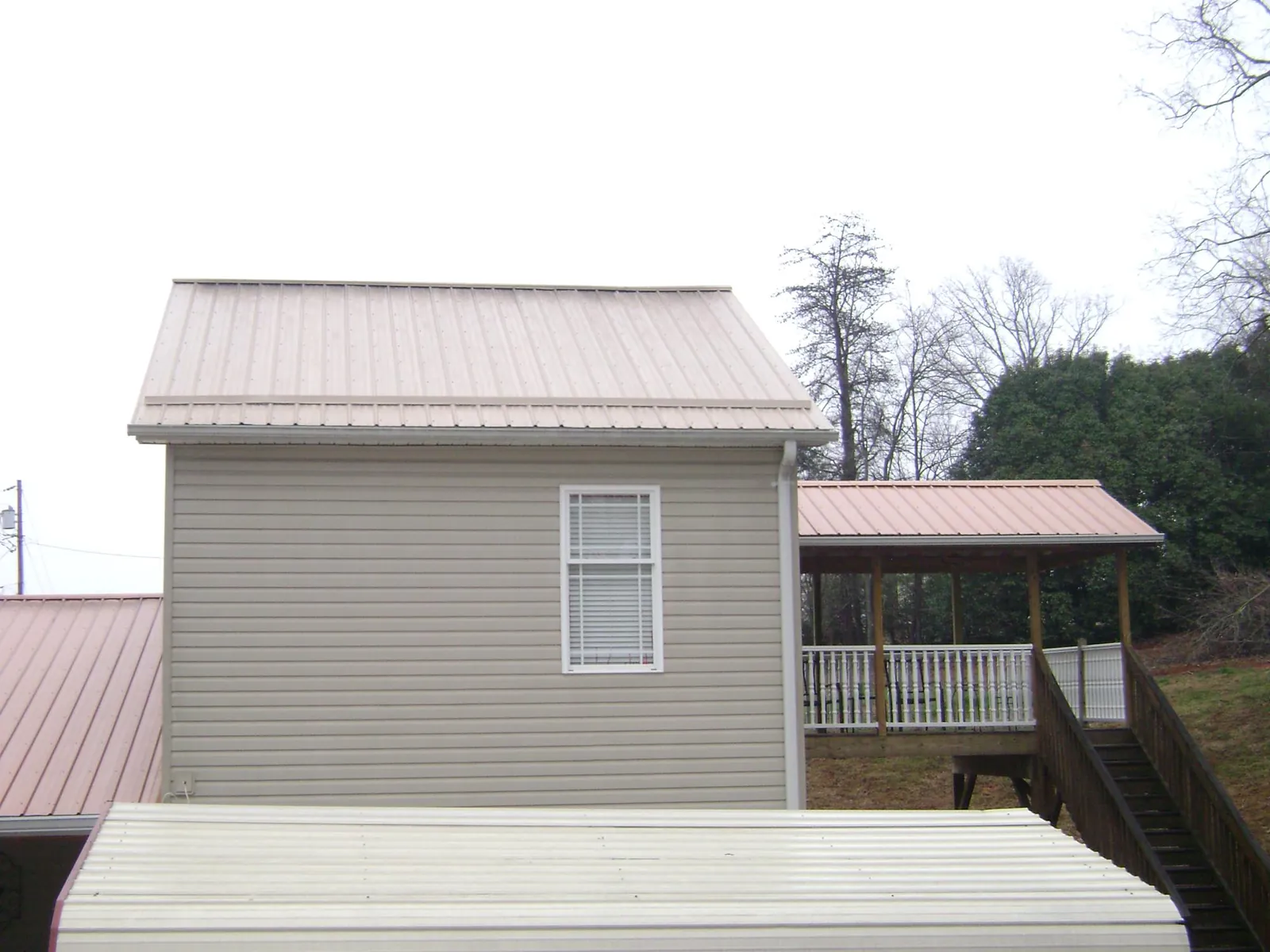 Tan metal roofs on a two story addition and attached porch, from a Roof Replacement job in Anvik